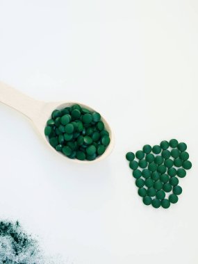 Yemek kaşıklarındaki yeşil Hawaii spirulinası tahta kaşıktaki haplar ve hapların kalbi. Süper yemek, sağlıklı yaşam tarzı, sağlıklı takviyeler, aşçılık konseptinde süper yiyecekler.