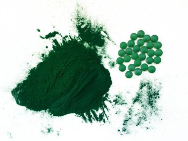 Masa kaşıklarıyla yeşil Hawaii spirulinası hapları ve açık beyaz arka planda toz. Süper yemek, sağlıklı yaşam tarzı, sağlıklı destek konsepti.
