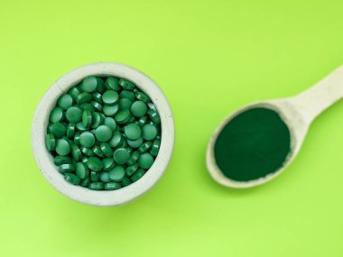 Masa kaşıklarında yeşil spirulina hapları ve açık yeşil arka planda toz. Süper yemek, sağlıklı yaşam tarzı, sağlıklı destek konsepti.