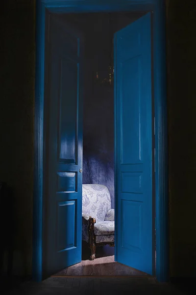 empty armchair in light behind blue massive vintage doors indoor. Old fashioned interior concept