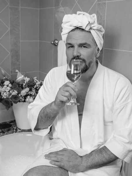 身穿白色浴衣 头戴毛巾 头戴白色浴衣的英俊而成熟的男人 同性恋 坐在浴室里 满身泡沫 喝着玫瑰酒 Spa Relax Lifestyle — 图库照片
