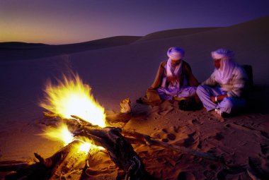 Tassili Najjer, Cezayir - 10 Ocak 2002: Cezayir Sahara kum tepeleri yangında ile gün batımında bilinmeyen erkekler, Afrika, Tassili Najjer Milli Parkı çöl