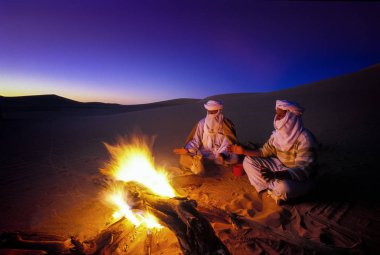 Tassili Najjer, Cezayir - 10 Ocak 2002: Cezayir Sahara kum tepeleri yangında ile gün batımında bilinmeyen erkekler, Afrika, Tassili Najjer Milli Parkı çöl