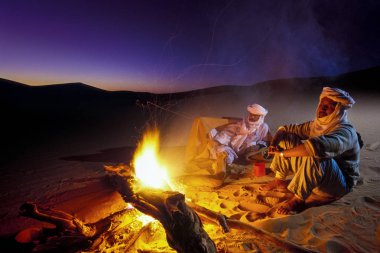 Tassili Najjer, Cezayir - 10 Ocak 2002: Cezayir Sahara kum tepeleri yangında ile gün batımında bilinmeyen erkekler, Afrika, Tassili Najjer Milli Parkı çöl