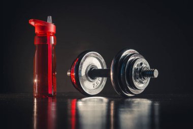 Kırmızı spor su şişesi ve halter koyu arka plan üzerinde
