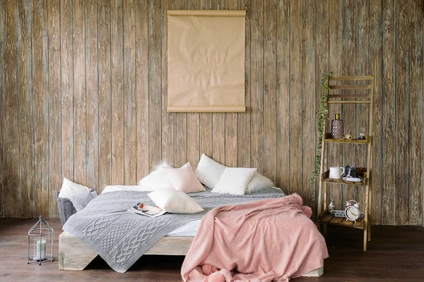 Bed for sleeping in the room. A wooden wall. Cozy and comfortable bed. Interior details: low bed, picture on the wooden wall, white pillows, pink blanket, gray plaid, candles.