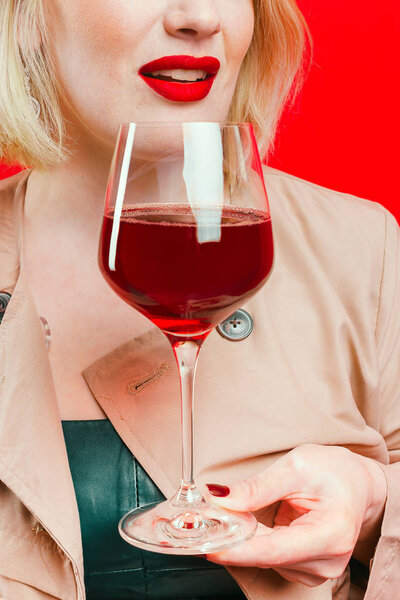 A glass of red wine in the hands of the girl. Red lipstick on lips. The girl is blonde. Close-up.