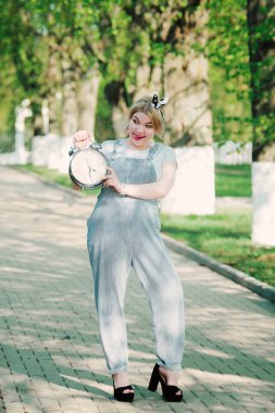 Kız ile bir masa saati (çalar saat) onun elinde. Sokak. Yeşil sokak. Zaman yönetimi. Kavramı.