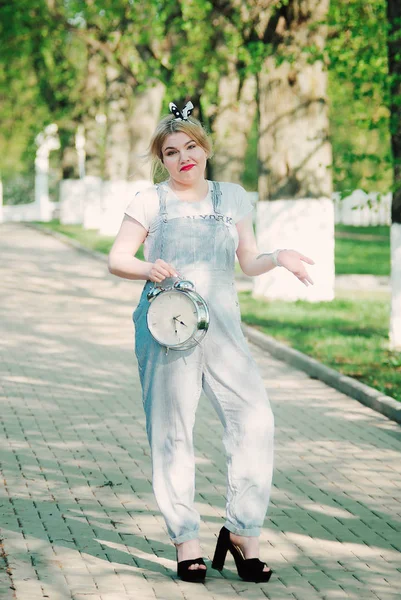 Kız ile bir masa saati (çalar saat) onun elinde. Sokak. Yeşil sokak. Zaman yönetimi. Kavramı.