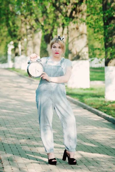 Kız ile bir masa saati (çalar saat) onun elinde. Sokak. Yeşil sokak. Zaman yönetimi. Kavramı.