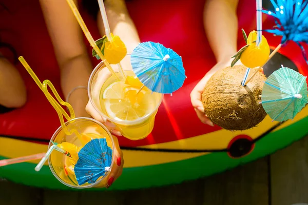 Summer citrus cocktails with umbrellas in the hands of girls. Refreshing lemonade. View from above. Bright color. Coconut drink.