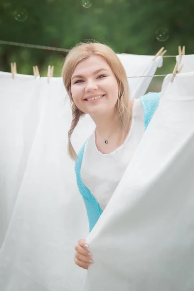 Young woman hangs white (clean) sheets in the garden. Domestic r