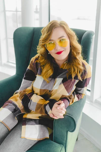 Young girl in yellow glasses sits on the armchair