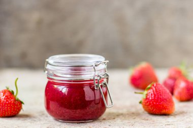 Masadaki cam kavanozda çilek reçeli.