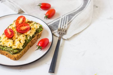 Omlet ve avokado ve kiraz domates ile kepekli ekmek üzerinde.