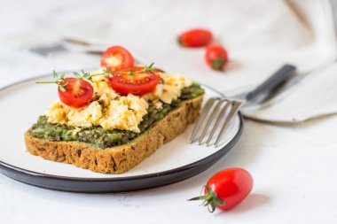 Omlet ve avokado ve kiraz domates ile kepekli ekmek üzerinde.