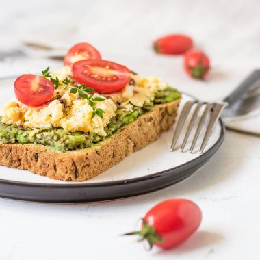 Omlet ve avokado ve kiraz domates ile kepekli ekmek üzerinde.