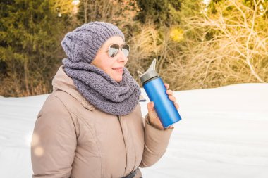 Yaşlı kadın üzerinden bir termos açık havada çay içer.