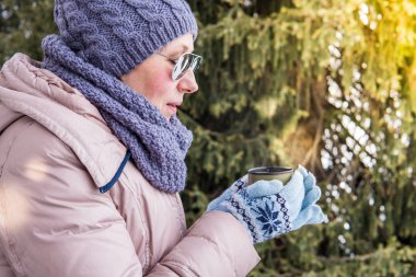 Yaşlı kadın üzerinden bir termos açık havada çay içer.
