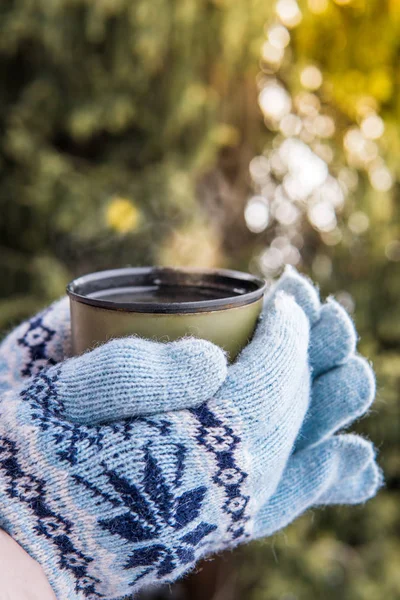 Cup of hot tea in the hands in gloves.