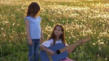 Şarkı ve akustik kot gitar dandelions sahada oynayan iki komik kız. küçük kızlar eğleniyor boş olarak açık havada