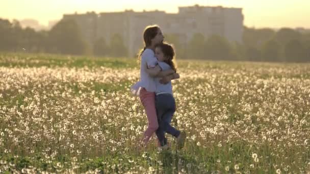 两个幸福的姐妹拥抱在城市建筑的背景下 在蒲公英的空地上盘旋 自由和无忧无虑 快乐童年 — 图库视频影像