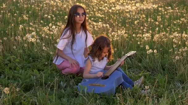 Two Little Cheerful Sisters Play Guitar Outdoors Dandelions Field Evening — Stock Video