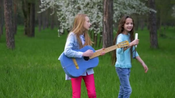 在森林公园模仿流行音乐音乐家的表演快乐的小女孩们在跳舞和唱歌的时候玩吉他 摇她的头发头 — 图库视频影像