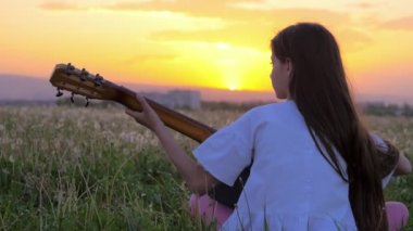 küçük genç kız gitar çalmak. gün batımında güzel yaz manzara. Sanat ve müzik kavramları. Dandelions alan şehrin. şehrin karmaşasından dinlenme