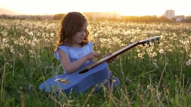 Милая Маленькая Девочка Сидит Траве Играет Джинсовой Гитаре Поле Одуванчиков — стоковое видео