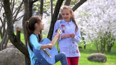 Mutlu ve pozitif iki müzik ve Doğa Park şarkı kız okul. bir genç kız çalış gitar diğer Çırp ellerini ve gülümsüyor