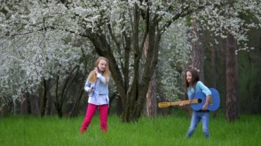 performans iki beyaz küçük kızlar açık havada bahar dalga. Orman maskaralıkları ve imitasyon pop müzisyenler akustik gitar rock müzik çalmak