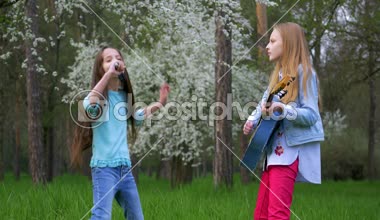 Sevimli Genç kız açık havada onun gitar çalmak. küçük kızlar saç ve birlikte dans şarkıları tarak şarkı