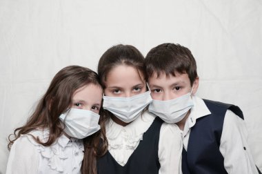 Coronavirus COVID-19 karantinası sırasında üç küçük çocuk maskeli ve okul üniformalı.