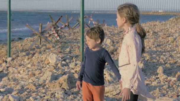 2人の貧しい孤児が海辺に立っているという概念です 難民キャンプの少年少女は家のない人生の絶望的な苦難から救われるのを待っています — ストック動画