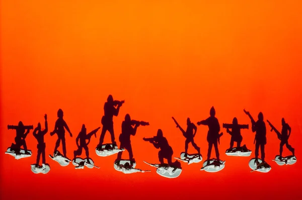 Group of armed toy soldiers with shadows fighting against each other on red orange sunset background — Stock Photo, Image