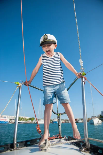 Arrabbiato piccolo ragazzo in cappello bianco capitano canotta a righe e pantaloncini jeans gridando su yacht di lusso mare in porto durante il viaggio di crociera estivo — Foto Stock