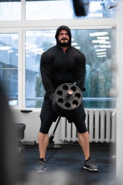 Spor salonunda elinde halter ve yüzünde çabayla genç sakallı bir adamın ağırlık kaldırma antrenmanında.