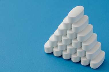 Birçok beyaz vitamin ilacı ilaç haplarından elde edilen piramit mavi saf yüzeyde fotokopi alanı ile birlikte