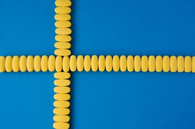 Mavi yüzeydeki sarı tabletlerin konsept sağlık hizmetleri ve İsveç bayrağında çapraz geçiş alanı