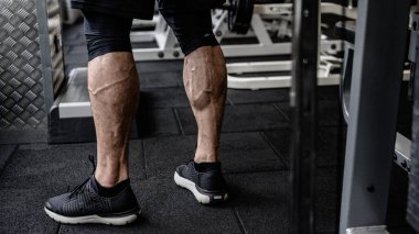 Spor ayakkabılarıyla spor salonunda spor aletlerinin yanında duran genç ve aktif erkek sporcuların güçlü buzağıları.