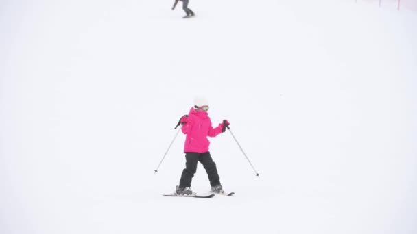 Liten flicka i rosa skiddräkt ridning på bergssluttningen under vintern snö semester fritid sport aktivitet — Stockvideo