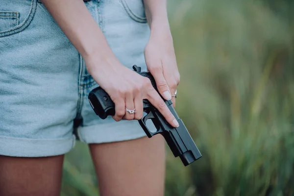 girl in denim shorts and with a gun in his hand posing in the field.