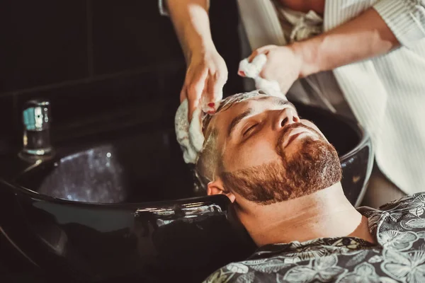 the barber washes the hair of a bearded man before a haircut