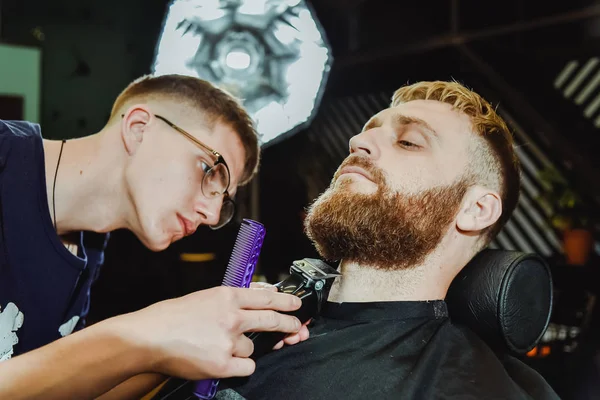 the barber cuts his beard to a man in the salon