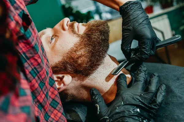 the barber shaves his beard with a man with a razor