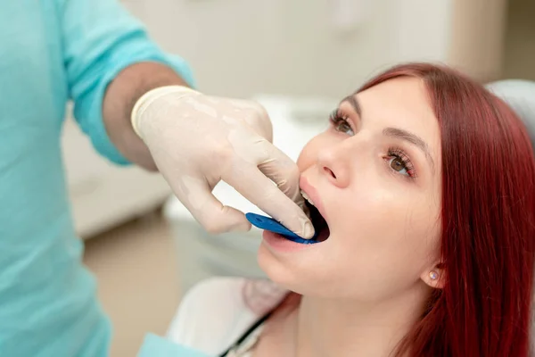 The orthodontist demonstrates to the girl patient the impression tray in which the silicone impression material will be placed to get the shape of her teeth..