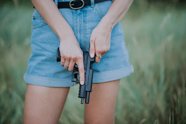 girl in denim shorts and with a gun in his hand posing in the field.