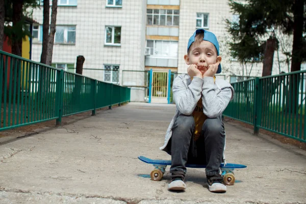 Um rapaz da cidade com um skate. O jovem de boné senta-se. Estilo urbano. Miúdos da cidade. O miúdo está a divertir-se. — Fotografia de Stock