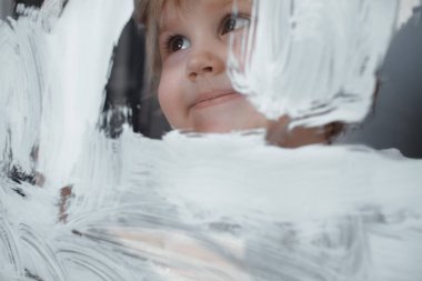 Çocuk cam bir tahtaüzerine beyaz bir boya çizer. Simüle ekran. Fırça ile mutlu çocuk